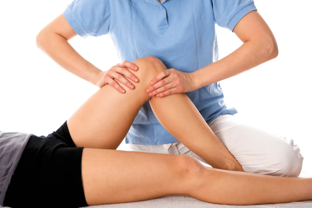 Physiotherapist in blue shirt performing knee joint therapy on a patient lying down, supporting and mobilizing the patient’s bent knee.