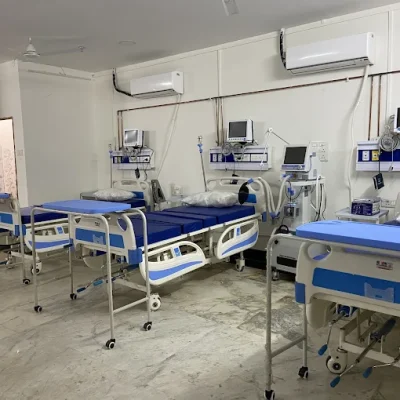 Empty hospital ward with multiple blue and white patient beds, pillows, medical monitors, and advanced equipment neatly arranged against the wall.